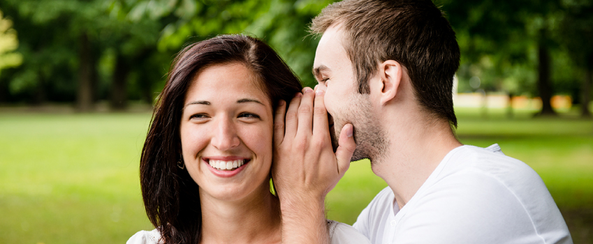 man whispering in woman's ear