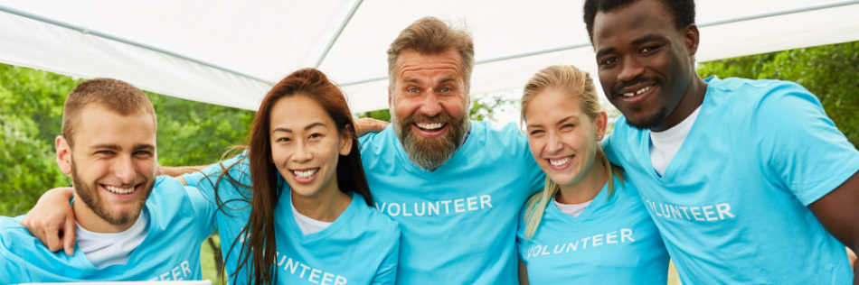 Group of volunteers smiling for a picture under a tent.